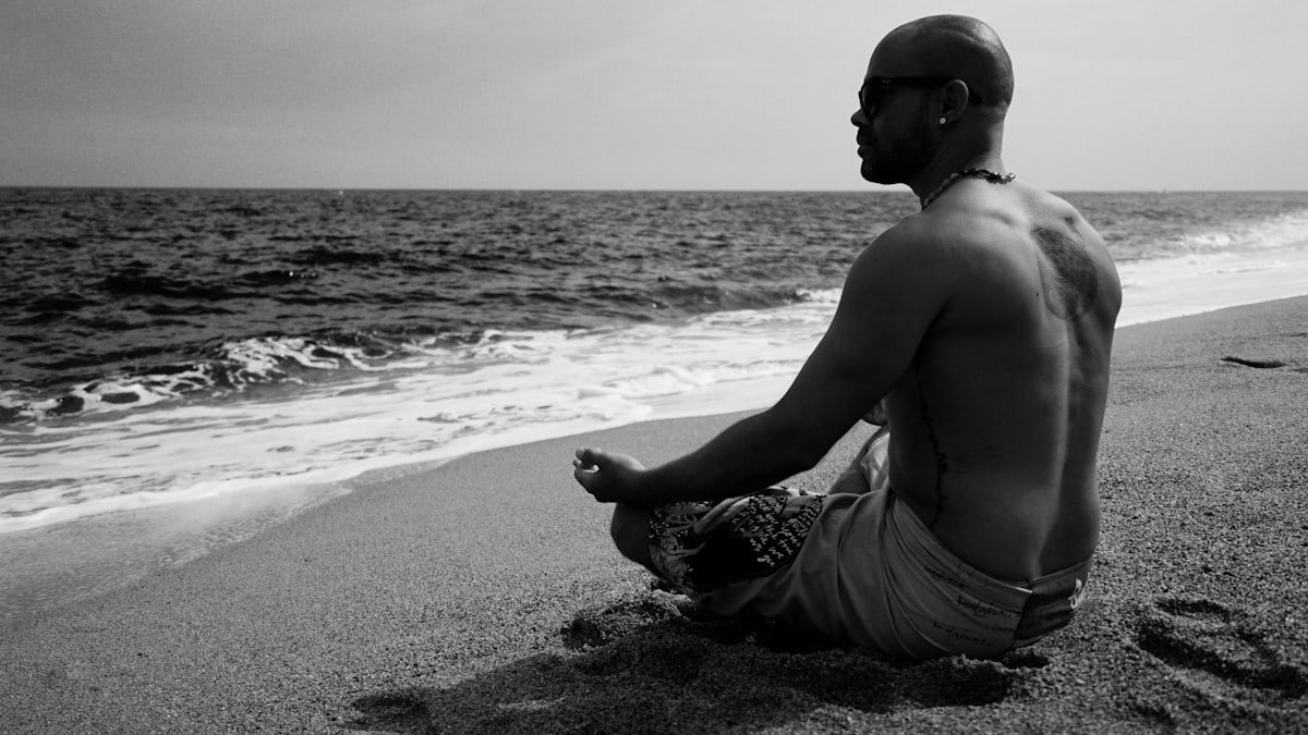 topless man in shorts sitting on beach shore